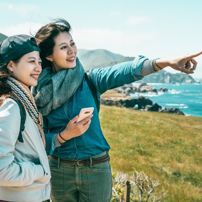 friends looking into ocean standing on coast close friends looking into the ocean and one girl pointing to somewhere with a phone held by a background of stunning coast.