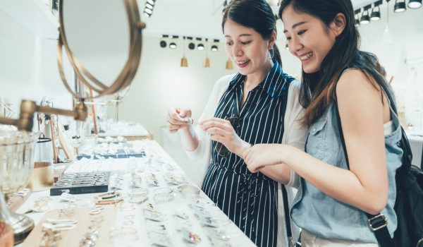 two asian women customers in busy clothes shop two asian women customer in busy clothes shop shopping accessories taking up from table. beautiful smiling young ladies best friends buying choosing earrings on desk in fashion modern store tokyo